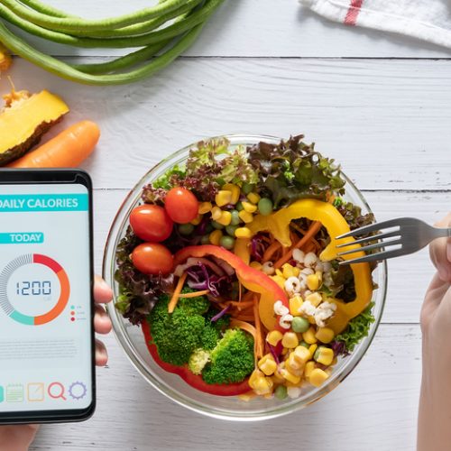 Calories counting , diet , food control and weight loss concept. Calorie counter application on smartphone screen at dining table with salad, fruit juice, bread and fresh vegetable. healthy eating